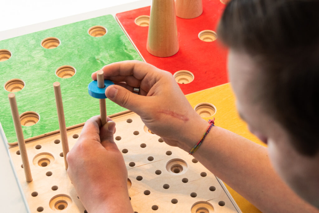 eine blaue Holzscheibe wird von mit zwei Händen auf ein Holfstab gesetzt