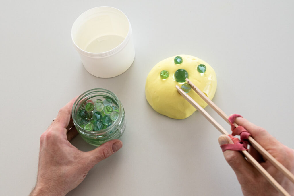 Murmeln die mit einer Holzzange auf eine Stück Knete gelegt werden